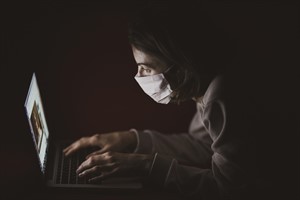 Woman wearing a mask working on a laptop